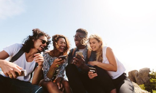 a group of friends sit outside laughing over their cell phones